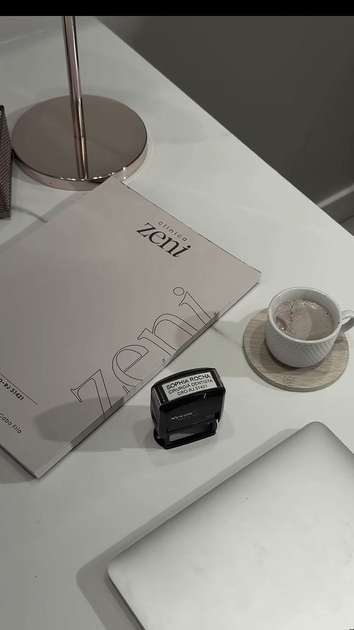 Mesa de atendimento da Clínica Zeni, com a pasta da clínica e um café